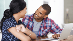 Supportive husband looking at his wife with encouragement while they review something together on a laptop—symbolizing belief, teamwork, and emotional connection in marriage.