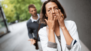 Woman wiping tears while partner stands behind, blurred, after an argument—illustrating marital pain and the need for safe repair.